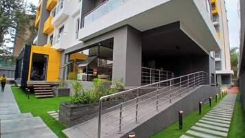 A modern building with a staircase leading to an upper level, surrounded by greenery and a well-maintained lawn.