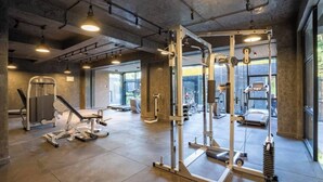 A gym with various exercise equipment, large windows, and a concrete ceiling. - Executive one Bedroom Kilimani (Nairobi)
