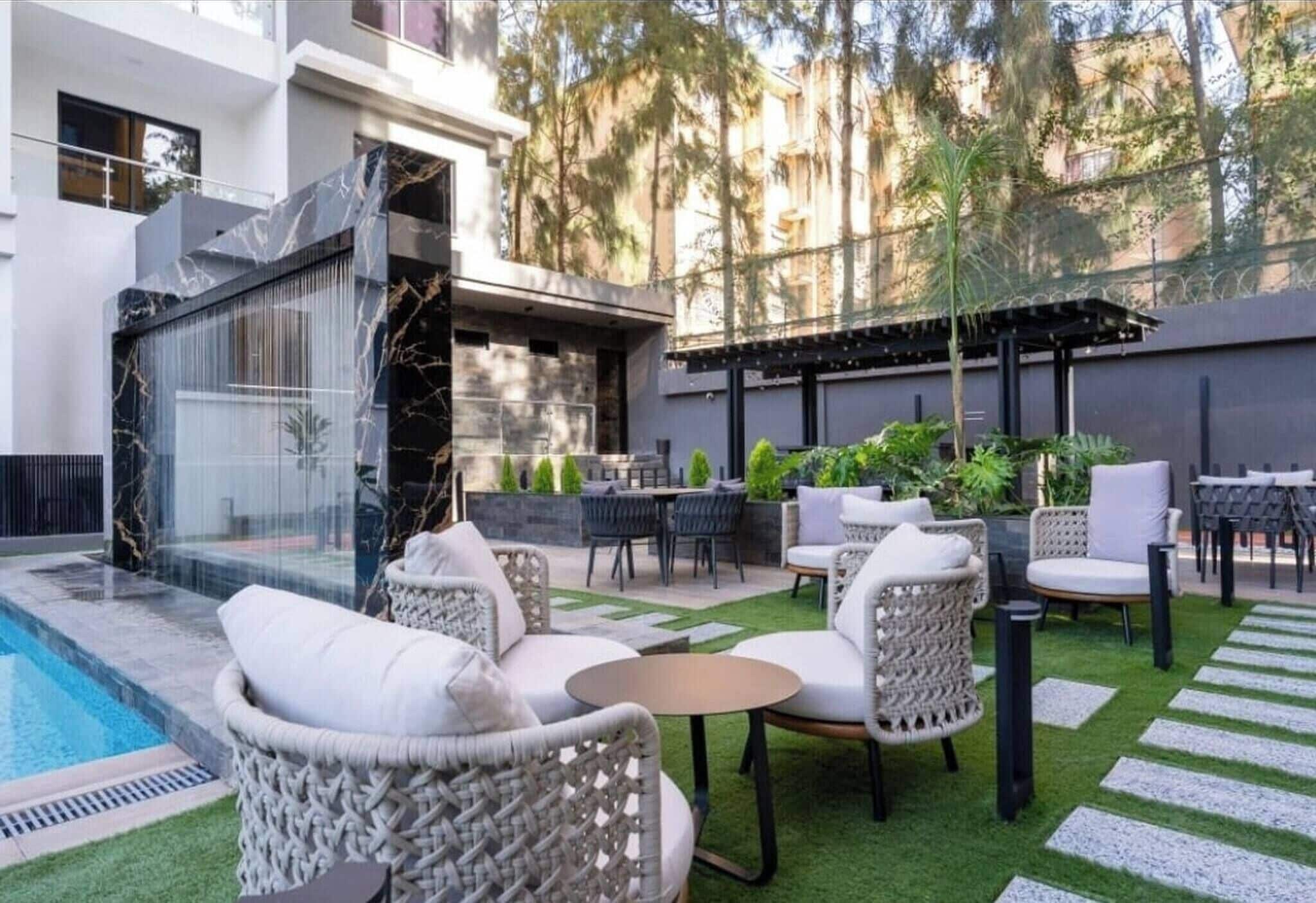 A modern outdoor patio with a pool, wicker furniture, and a pergola.
