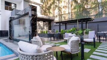 A modern outdoor patio with a pool, wicker furniture, and a pergola.