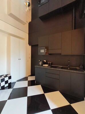 A modern kitchen with a black and white checkered floor, dark cabinetry, and a microwave. - The Rabbit Hole: Unique Design Stay in Milan Downtown with AC and Wifi (Milano)
