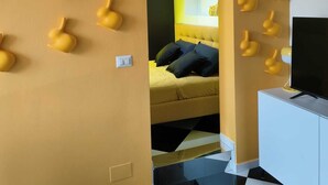 A room with a checkered floor, a bed with dark bedding, a TV on a white cabinet, and a wall with multiple wall-mounted light fixtures. - The Rabbit Hole: Unique Design Stay in Milan Downtown with AC and Wifi (Milano)
