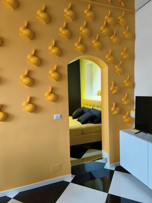 A room with a checkered floor, a bed with dark bedding, a TV on a white cabinet, and a wall with multiple wall-mounted light fixtures. - The Rabbit Hole: Unique Design Stay in Milan Downtown with AC and Wifi (Milano)