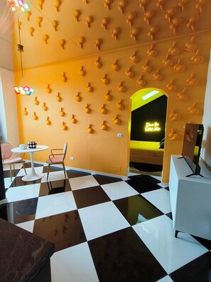 A room with a checkered floor, a wall with a pattern of spherical objects, a neon sign, and a small table with chairs. - The Rabbit Hole: Unique Design Stay in Milan Downtown with AC and Wifi (Milano)