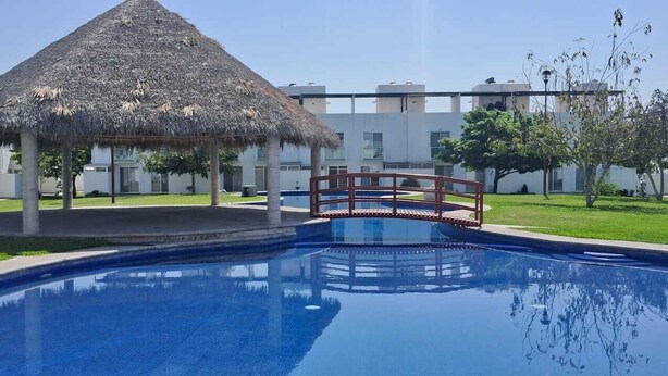 A swimming pool with a thatched-roof structure and a bridge, surrounded by modern buildings. - Family retreat: Relaxation and disconnection (Yautepec)