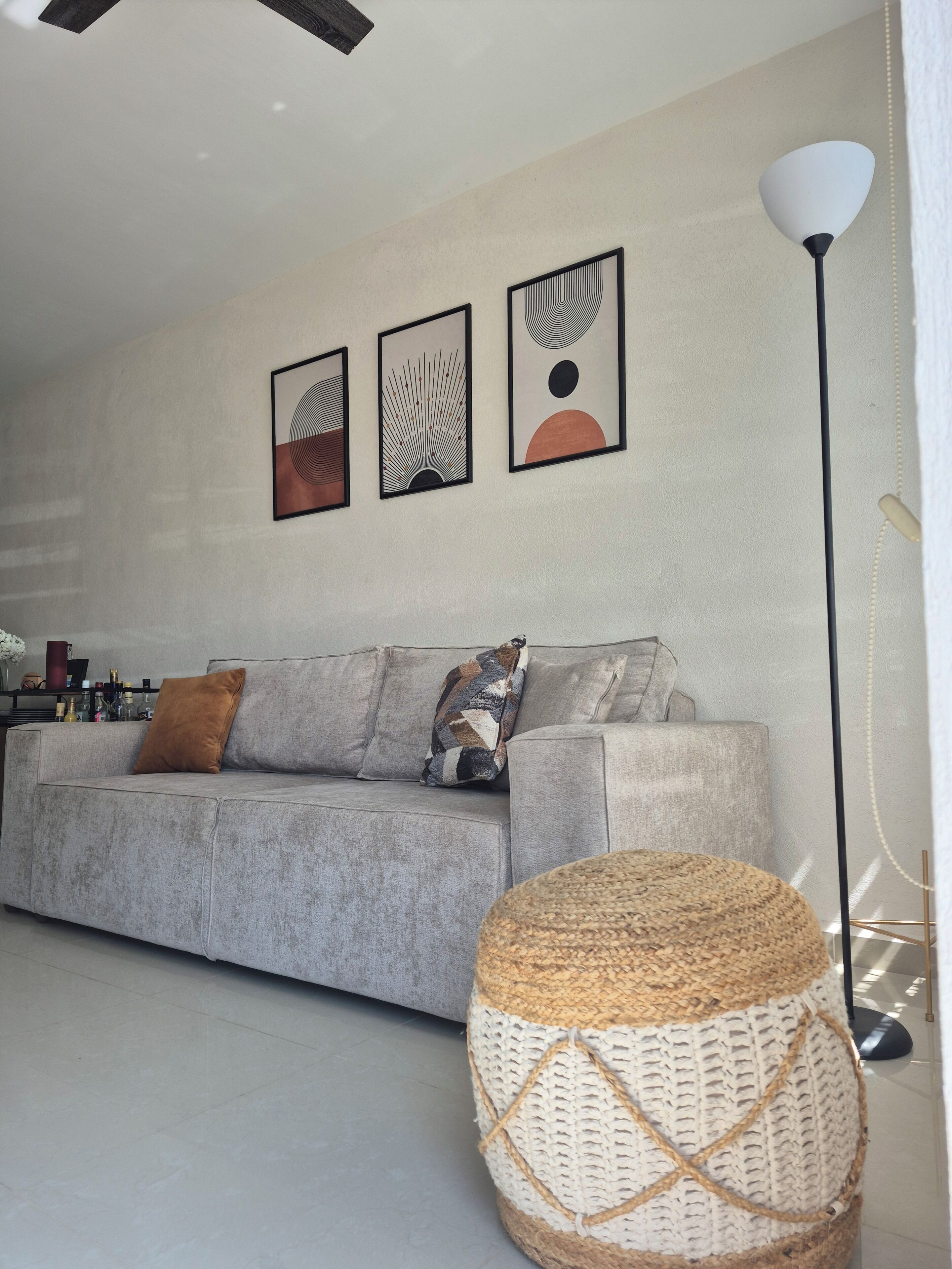 A living room with a grey sofa, three framed artworks, a floor lamp, and a woven basket.