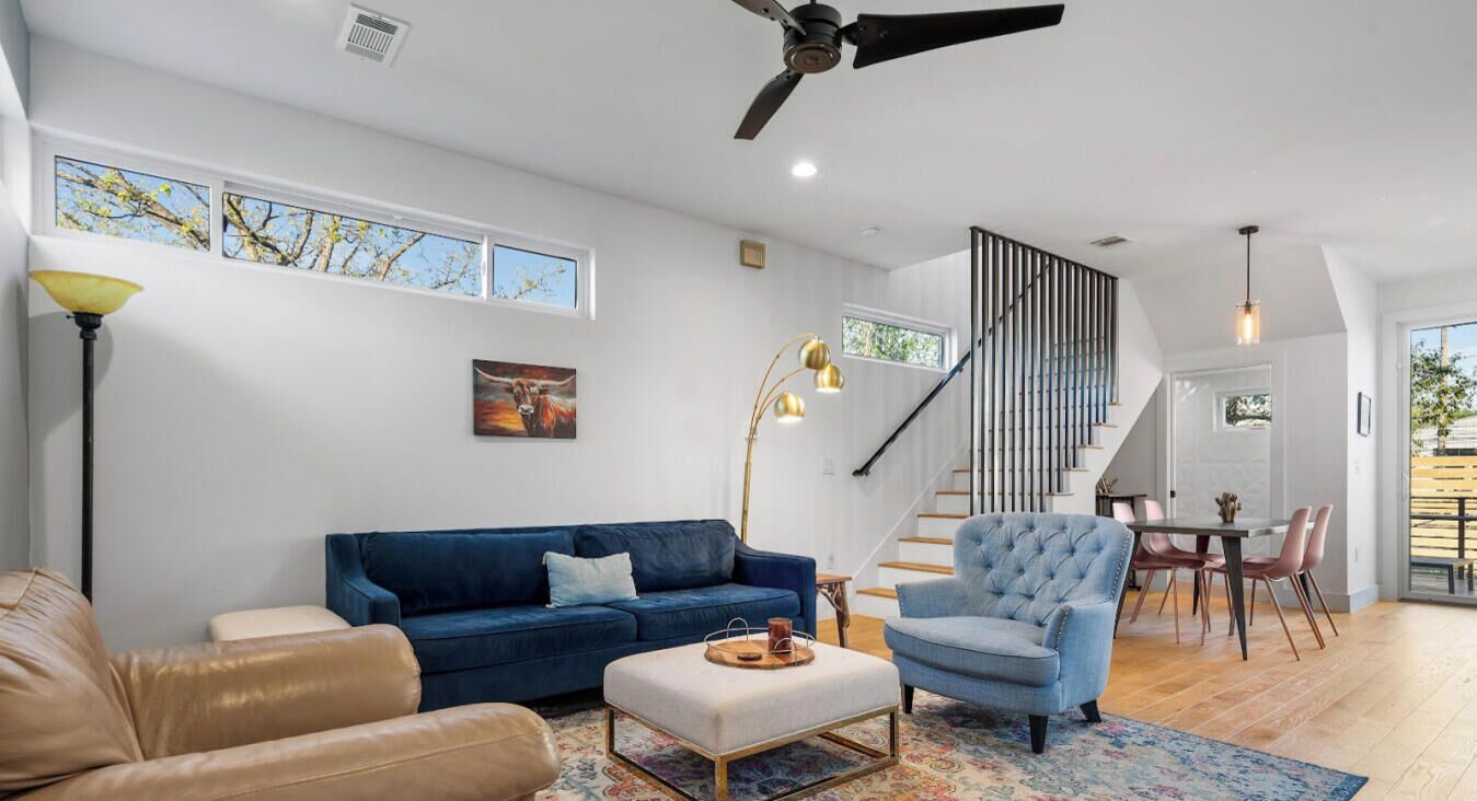 A modern living room with a blue sofa, a leather armchair, a blue armchair, a coffee table, and a staircase with a railing.