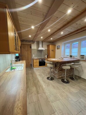 A kitchen with wooden cabinets, a built-in oven, a sink, and a bar area with stools. - Vacation home Swinoujscie with sauna and whirlpool (Tönning)