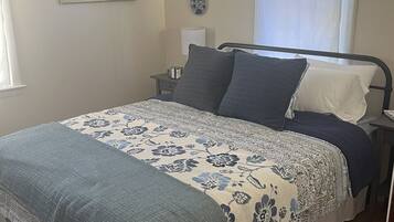 A bedroom with a bed, a nightstand, a window, and a painting on the wall.