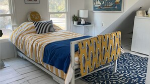 Un dormitorio con cama, mesita de noche, lámpara, cuadro y ventana.