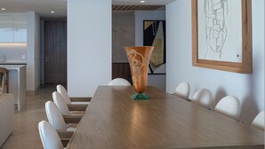 A conference room with a wooden table, white chairs, a vase, and a framed abstract painting. - Spectacular Kupuri Beach Oceanfront 6BR Luxury Villa, Infinity Pool, Chef (Punta Mita)