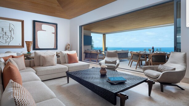 A modern living room with a large window, a sofa, a coffee table, and a dining area with a view of the ocean. - Spectacular Kupuri Beach Oceanfront 6BR Luxury Villa, Infinity Pool, Chef (Punta Mita)