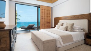 A bedroom with a large bed, a wooden headboard, a bench, and a view of the ocean. - Spectacular Kupuri Beach Oceanfront 6BR Luxury Villa, Infinity Pool, Chef (Punta Mita)