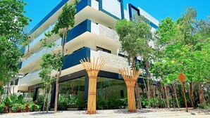 Un bâtiment moderne à plusieurs étages, doté d’un toit plat, entouré d’une végétation luxuriante et de structures en bambou.