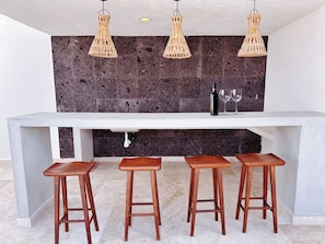 A kitchen with a white countertop, three wooden stools, and three wicker pendant lights. - Centric 2BD Condo in Aldea Zama (Tulum)