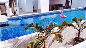 Une piscine sur le toit, agrémentée d’un flotteur en forme de flamant rose, de palmiers et d’un bâtiment blanc avec une clôture en bois.