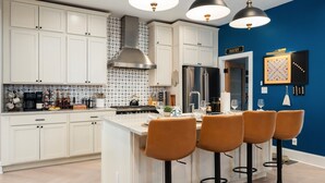 A modern kitchen with white cabinets, a stainless steel range hood, and a blue accent wall. - Pregame Palace | Hot Tub • HGTV • Garage Parking • Pets (Indianapolis)