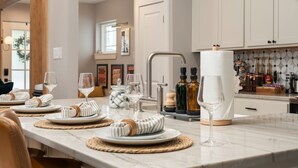 A modern kitchen with marble countertops, a central island, and a bar area with bottles and glasses. - Pregame Palace | Hot Tub • HGTV • Garage Parking • Pets (Indianapolis)