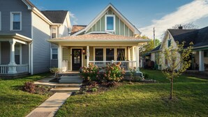 A two-story house with a front porch, a small garden, and a clear sky. - Pregame Palace | Hot Tub • HGTV • Garage Parking • Pets (Indianapolis)