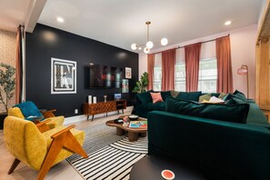 Una sala de estar moderna con una pared oscura, un sofá verde, un sillón amarillo, una mesa de centro de madera y un televisor montado en la pared.