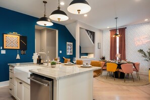 Una cocina moderna con una isla central, un comedor con mesa redonda y una escalera que sube a un nivel superior.