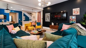 A modern living room with teal sofas, a coffee table, and a TV wall-mounted above a dark wall. - Pregame Palace | Hot Tub • HGTV • Garage Parking • Pets (Indianapolis)