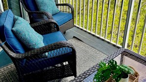 A balcony with wicker furniture, a potted plant, and a view of a green landscape. - Anna Maria Island -walk to the beach, shops and restaurants! (holmes Beach)