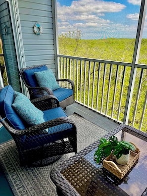 Ein Balkon mit Korbmöbeln, einem Blumentopf und Blick auf eine grüne Landschaft.