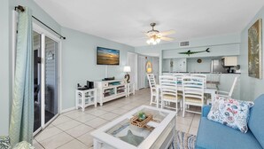 A living room with a glass coffee table, white furniture, a ceiling fan, and a dining area with chairs and a table. - Anna Maria Island -walk to the beach, shops and restaurants! (holmes Beach)