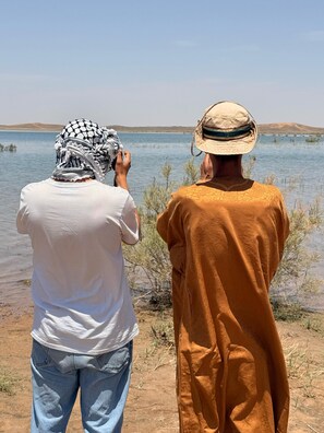 Two people standing by a lake with a distant hill.