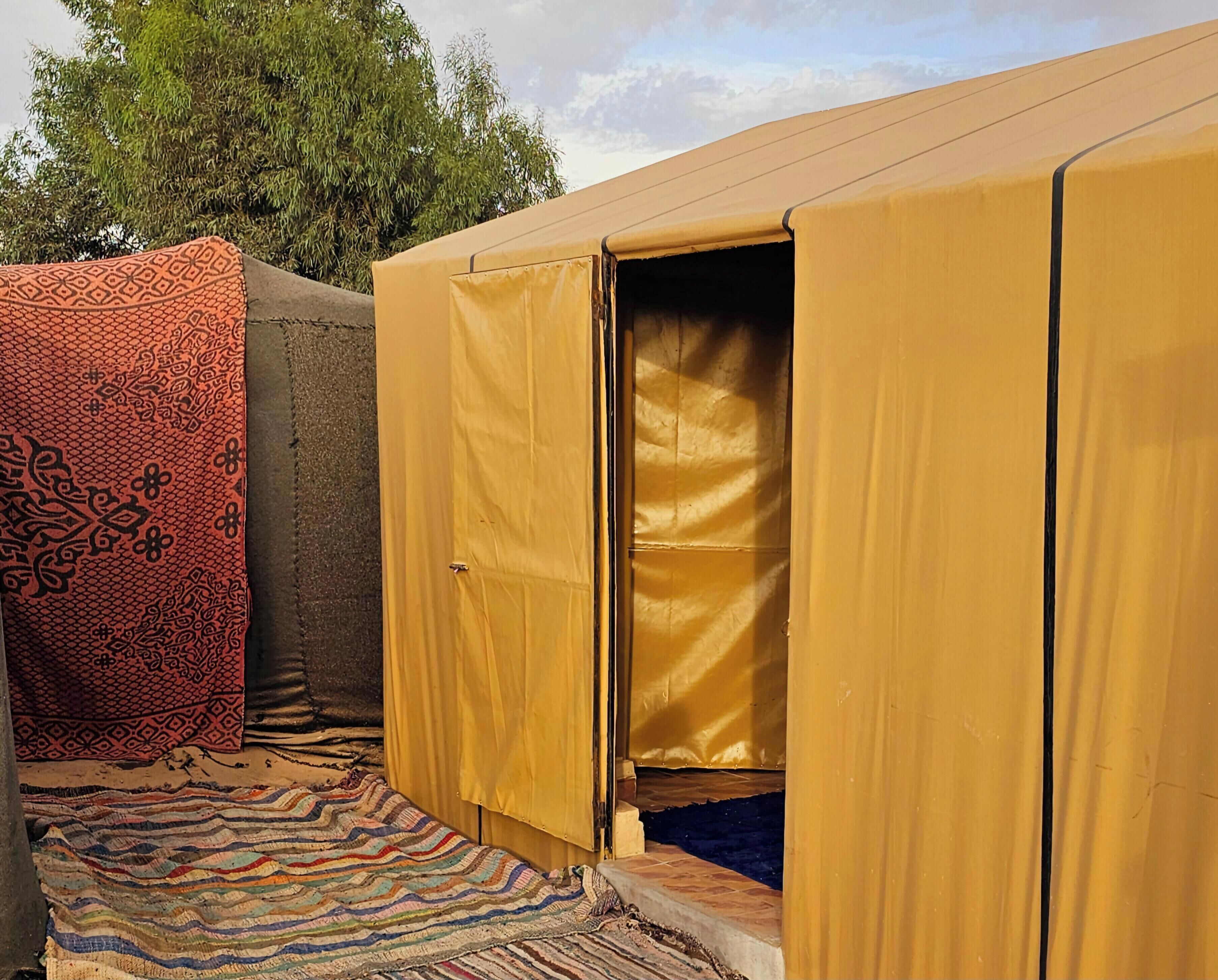 A tent with an open door, a patterned fabric, and a striped rug.
