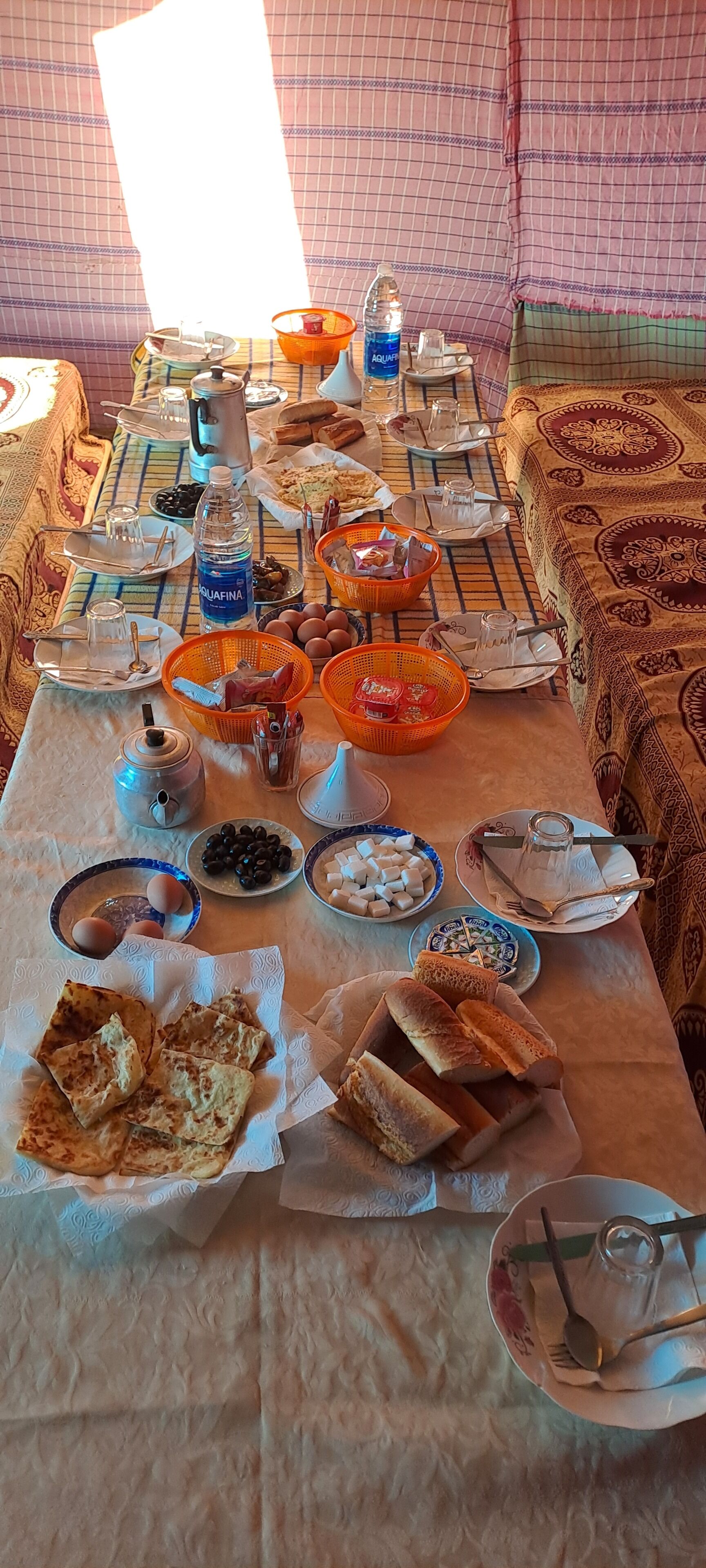 Une table à manger avec divers aliments et ustensiles, une bouteille d’eau et une bouilloire.