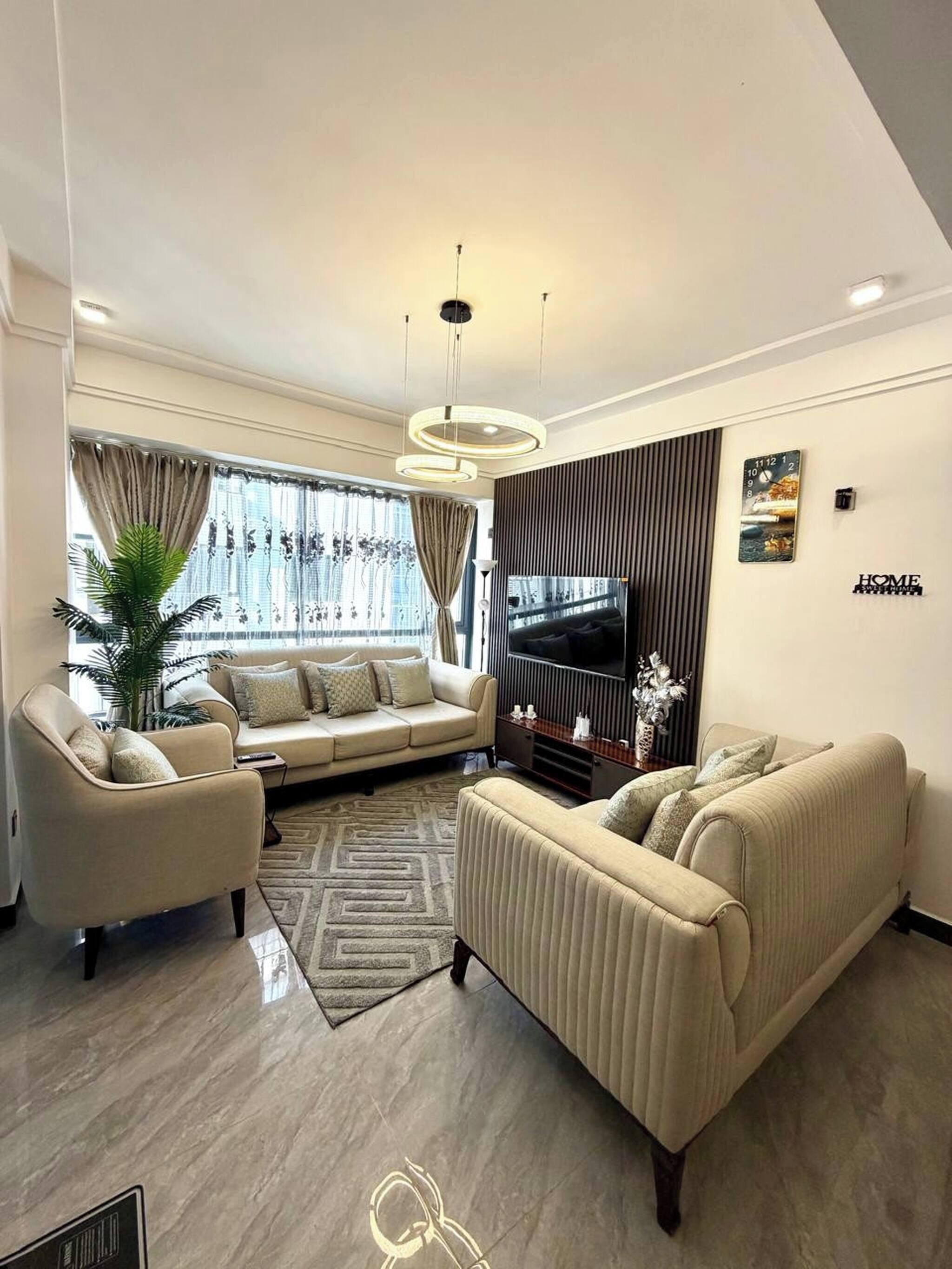 A modern living room with a sofa, armchairs, a TV, and a decorative wall piece.