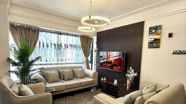 Ein modernes Wohnzimmer mit einer Couch, Sesseln, einem Fernseher und einer Wanddekoration.