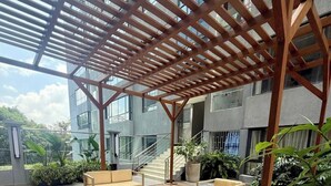 Eine hölzerne Terrasse im Freien mit Sitzgelegenheiten, einer Pergola und Blick auf ein modernes Gebäude.