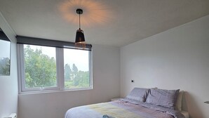 Een slaapkamer met een bed, een raam, een radiator en een nachtkastje.