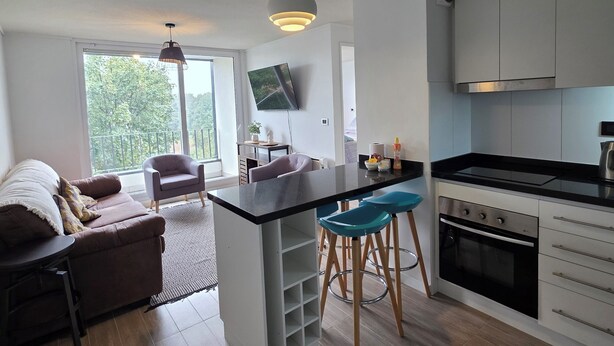 Een moderne keuken met een centraal eiland, barstoelen, een inbouwoven en een flatscreen televisie.