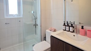 Een moderne badkamer met een douchecabine van glas, een wit toilet, een wastafelmeubel met een spiegel en een wastafel.