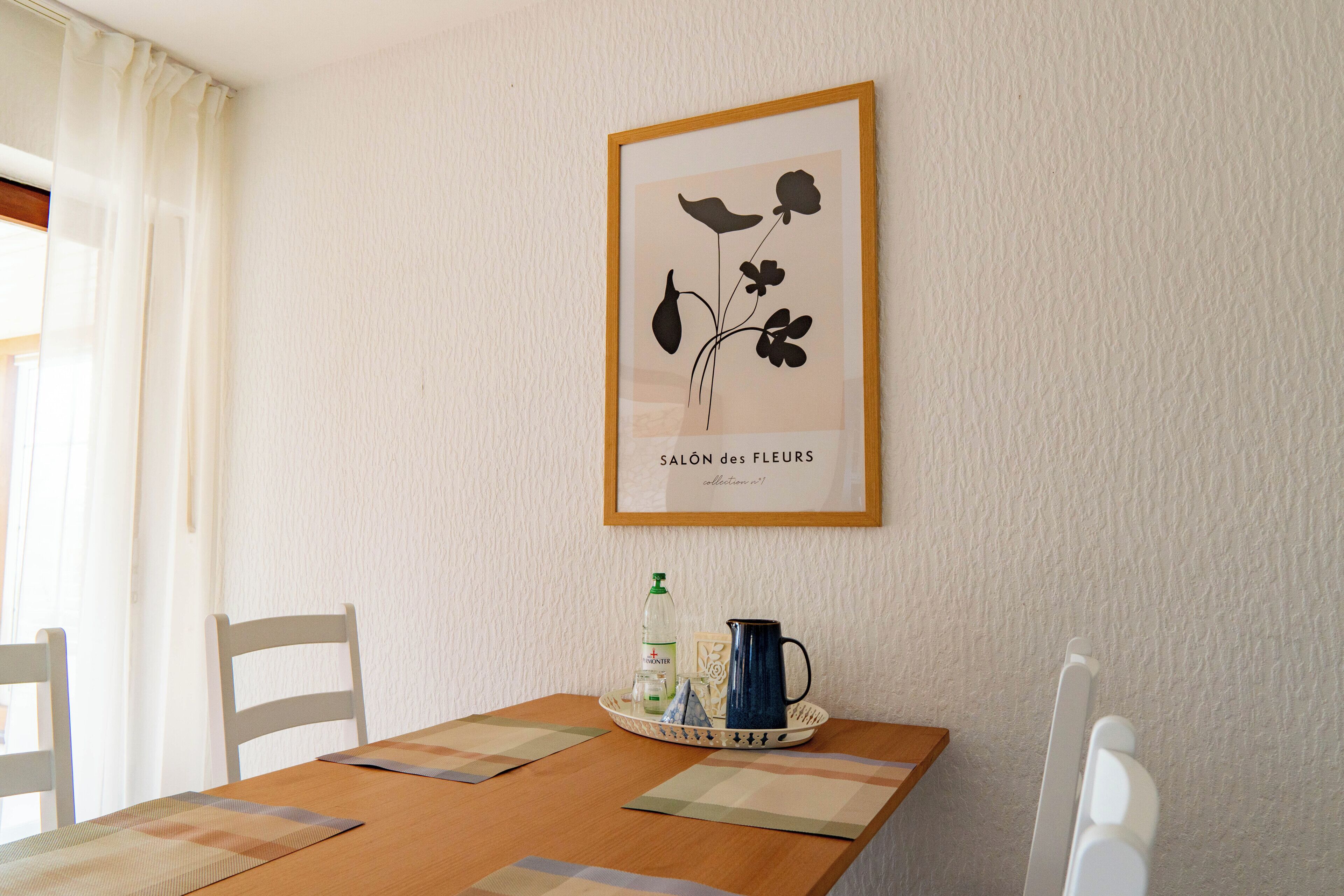 Ein Esstisch mit einem gerahmten Kunstwerk, einer Karaffe, einer Flasche und einem Tablett.