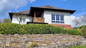 Uma casa de dois andares com uma parede de pedra em frente, um deck de madeira e uma janela grande.