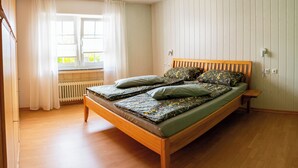 Uma cama de solteiro com estrutura de madeira, colchão verde e roupa de cama estampada com flores.