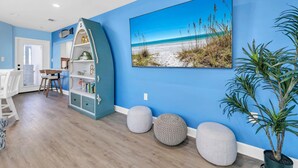 Una habitación con pared azul, un cuadro con motivos marinos, un mueble blanco y una planta en maceta.