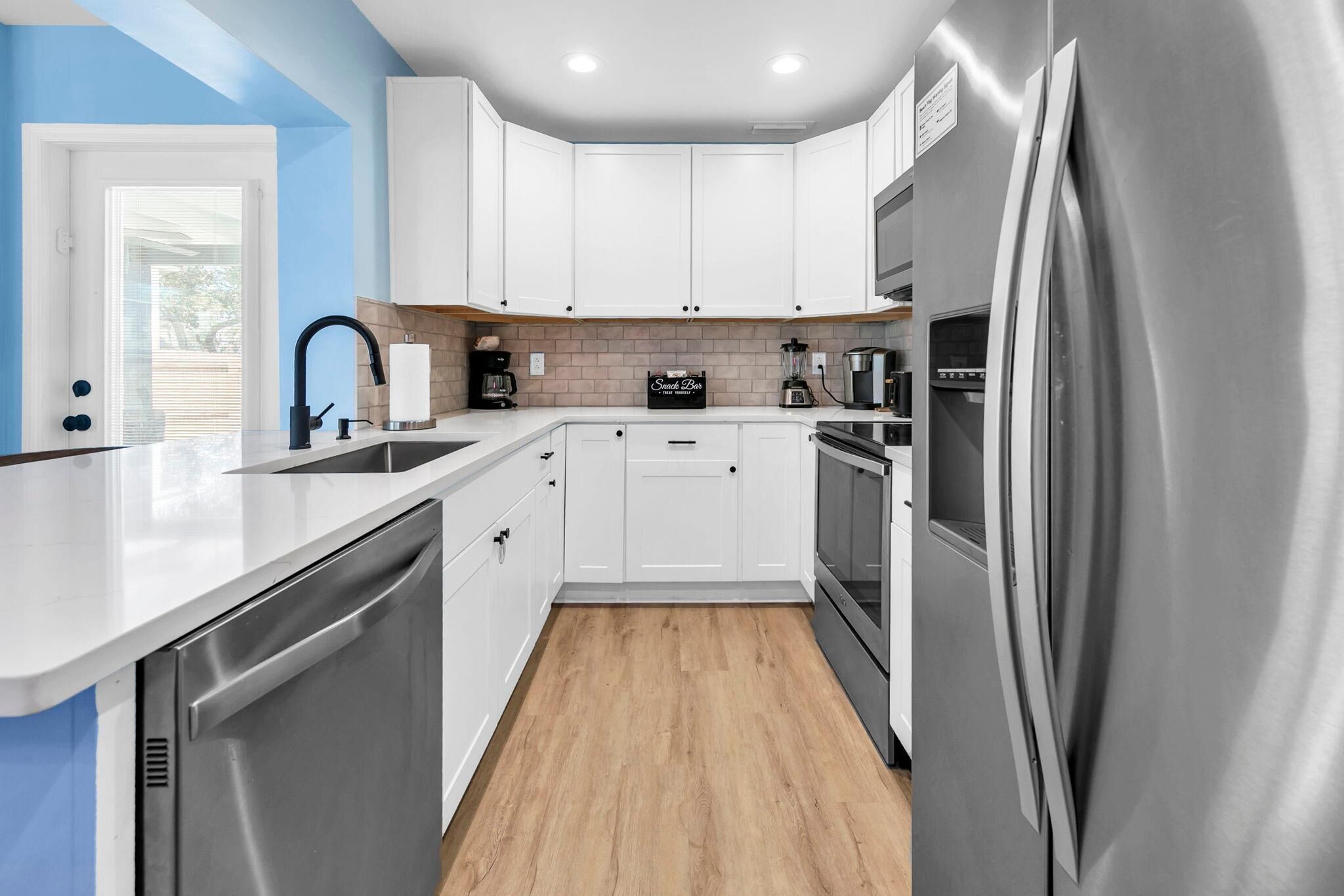 Una cocina moderna con armarios blancos, electrodomésticos de acero inoxidable y piso de madera.