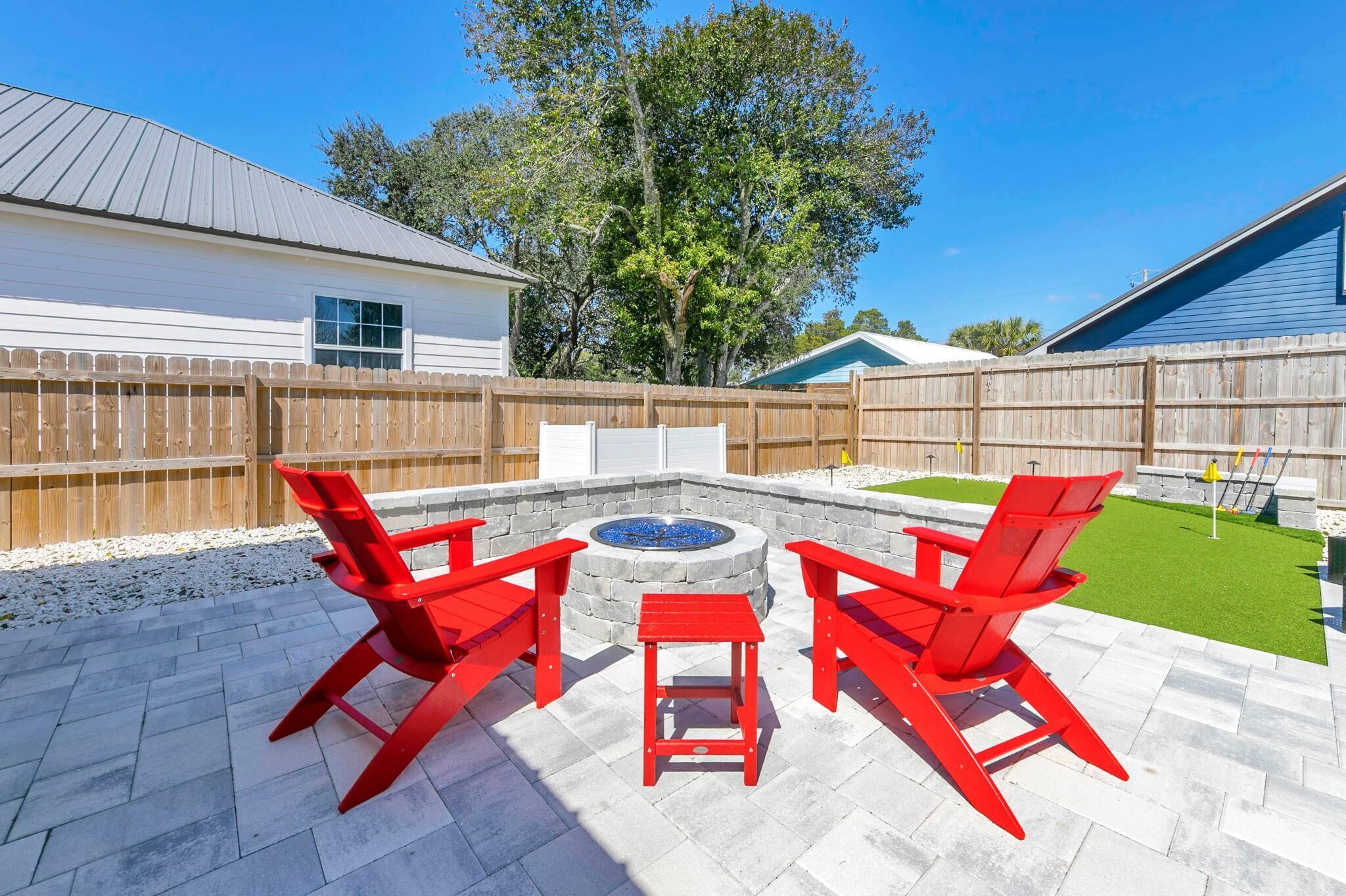 A backyard with a stone fire pit, red chairs, and a herringbone-patterned patio.