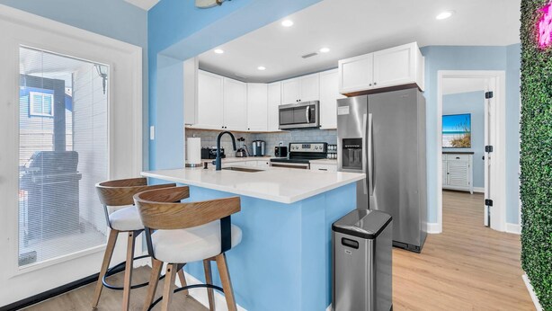 Una cocina moderna con armarios blancos, electrodomésticos de acero inoxidable y una isla central con taburetes de bar.