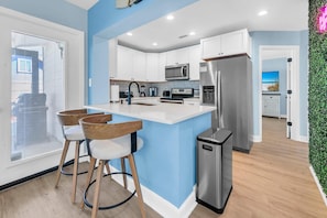 A modern kitchen with white cabinets, stainless steel appliances, and a central island with bar stools. - The White Sandcastle (Panama City Beach)
