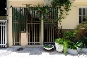 A building entrance with a metal gate, a potted plant, and a number '51' on the wall. - One-bedroom apartment with living room, house style, affordable in Ipanema! (Rio de Janeiro)