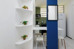 A compact kitchen with white shelves, a microwave, a refrigerator, and two stools. - One-bedroom apartment with living room, house style, affordable in Ipanema! (Rio de Janeiro)