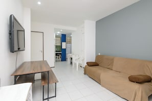 A living room with a sofa, a TV, a table, and a kitchen area in the background. - One-bedroom apartment with living room, house style, affordable in Ipanema! (Rio de Janeiro)