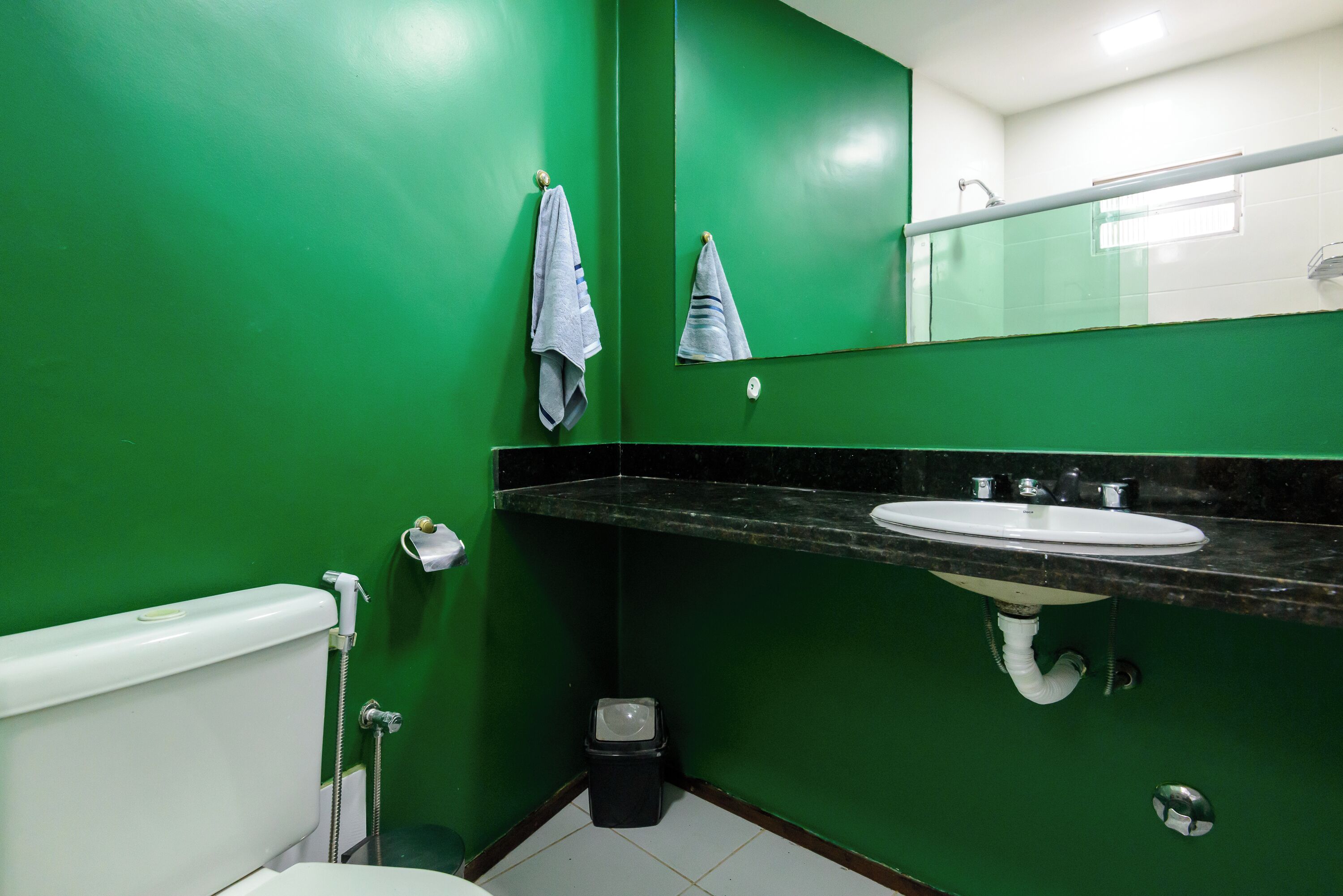 A bathroom with green walls, a white toilet, a sink with a black countertop, and a mirror above the sink.